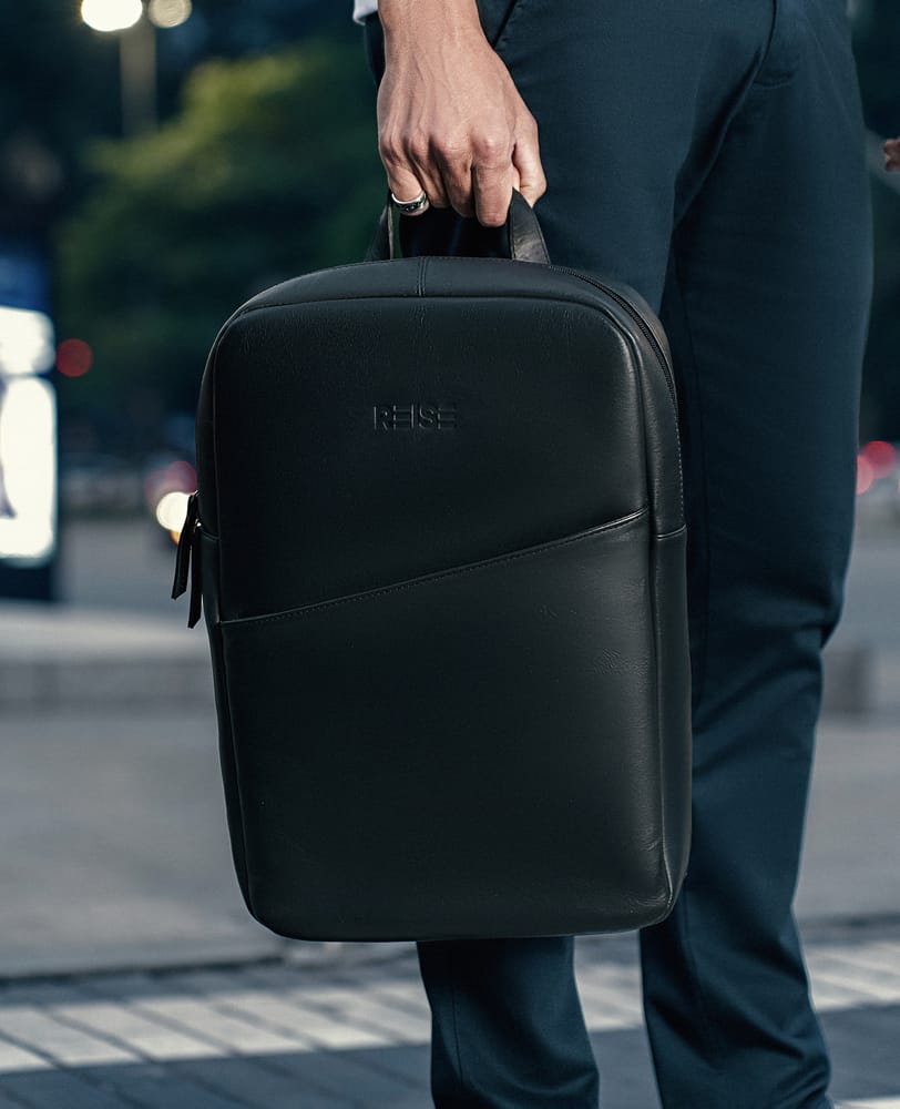 Mochila Slim Couro Preta e NYC Modelo Segurando Alca